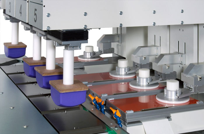 A pad printing machine with multiple blue silicone pads and cliche plates aligned for printing.